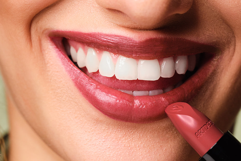 Lips with applied lipstick are shown with a lipstick held in front of the face