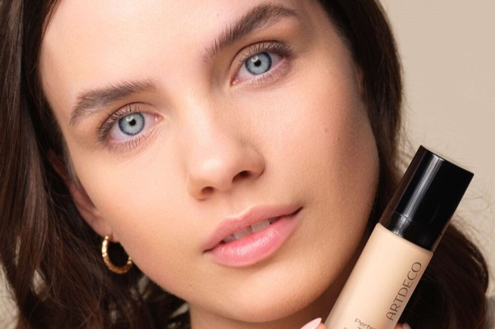 Model looks neutrally into the camera with her head slightly tilted to the left while holding the Perfect Teint Foundation.