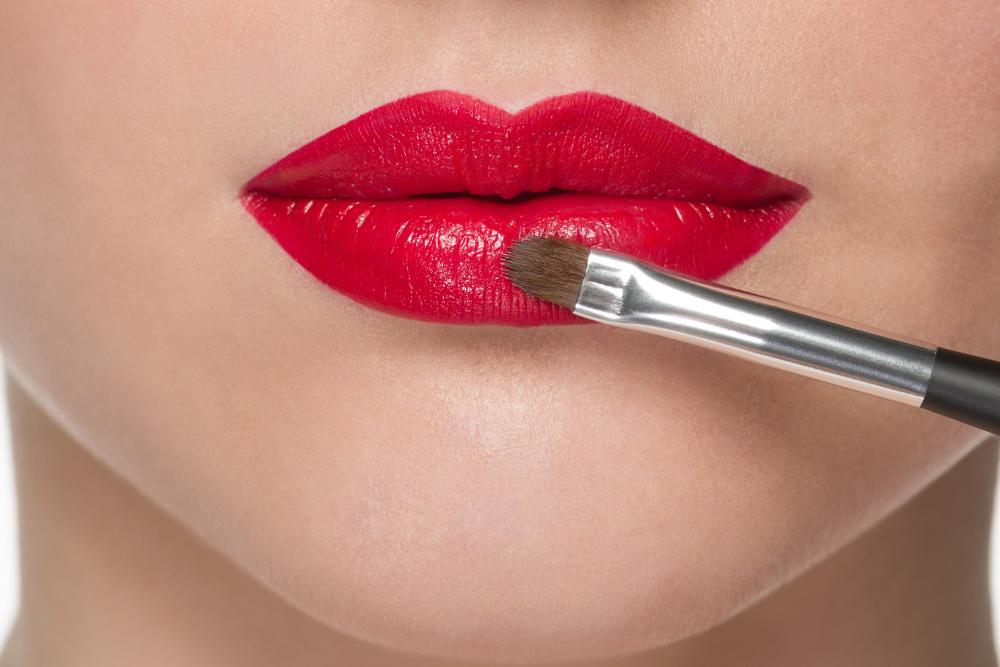 Red lipstick is applied to the lips using a lip brush.