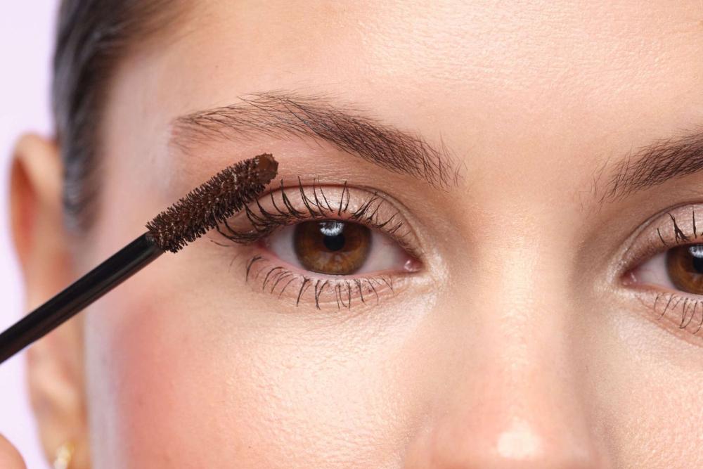 A woman with made up eyes holding one mascara brush in front of her face