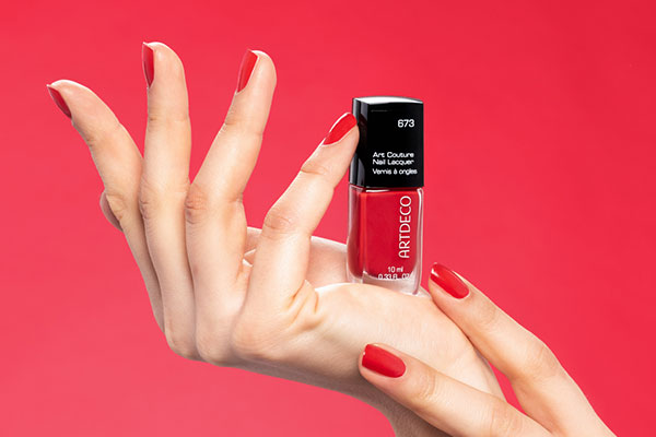 A hand is shown on which a red nail polish is presented
