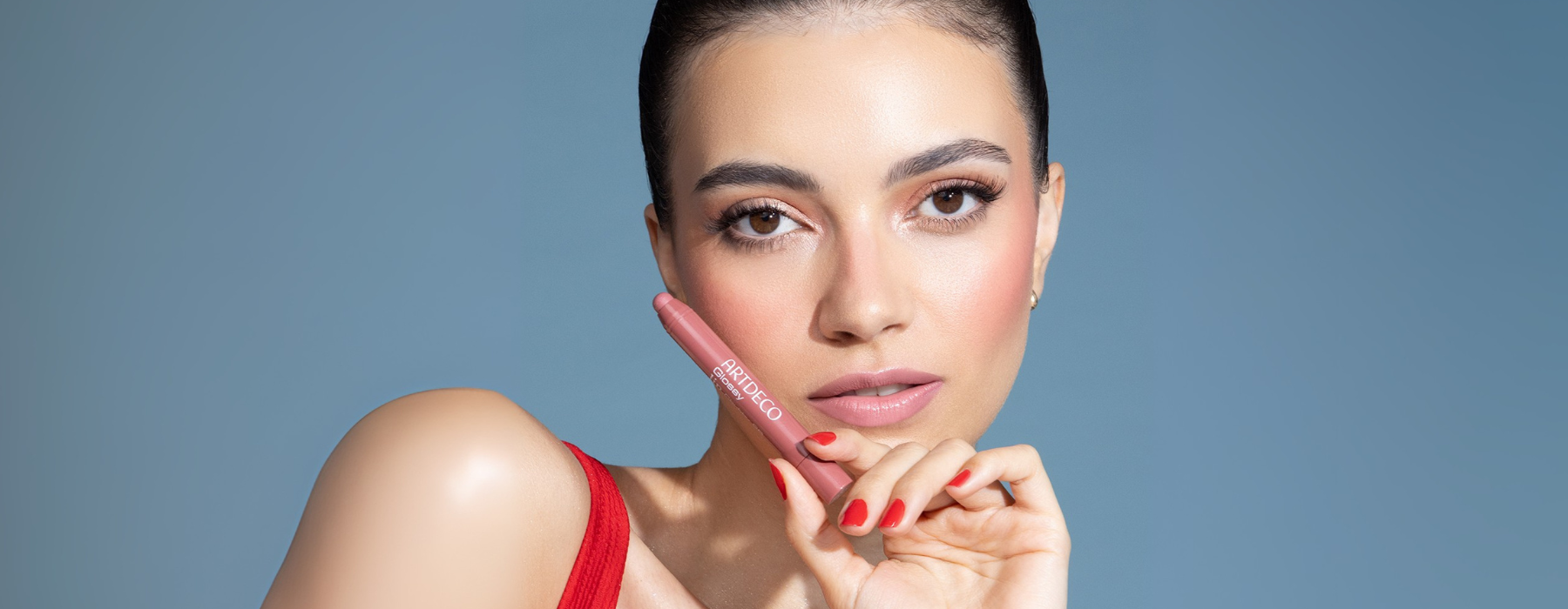 Brunette model holds one of the ARTDECO Glossy Lip Chubby in her hand. Her fingernails are painted in a summery red