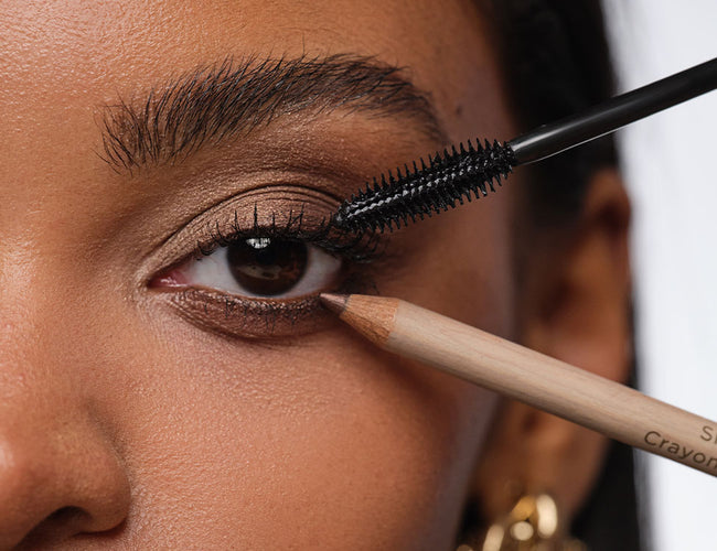 Close up on the open eyes of the model; a Kajal Liner is being held to the lower lash line and mascara is being held to the upper lash line