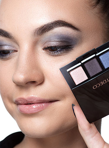 A model holds an eyeshadow palette next to her finished eye makeup.