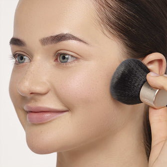 Woman in profile gets powder applied with kabuki brush