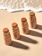 Bronzer sticks placed in a row on a beach background.