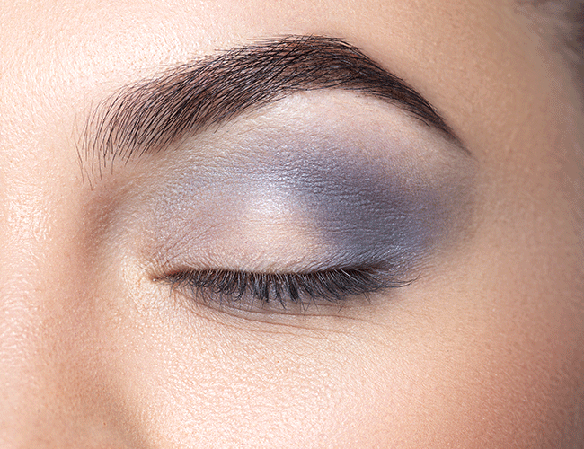 Blue eyeshadow is applied to the outer eyelid and lower lash line using a fluffy brush.