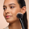 Woman with bronzed complexion poses with a bronzer next to her face
