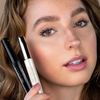 Model holds various mascaras to her cheek and has beautifully mascaraed eyelashes