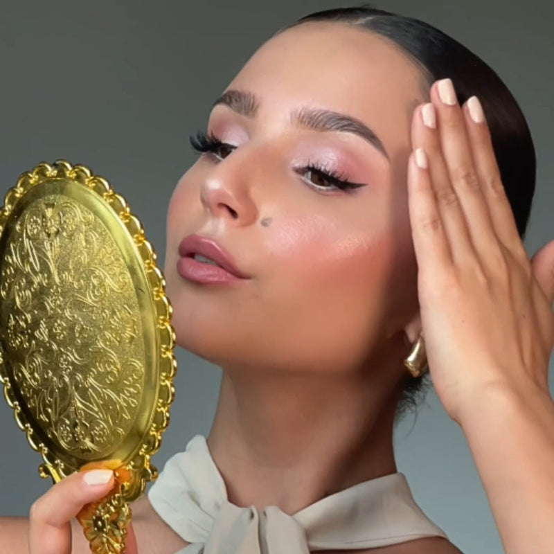 A model wearing makeup looks at herself in a mirror.