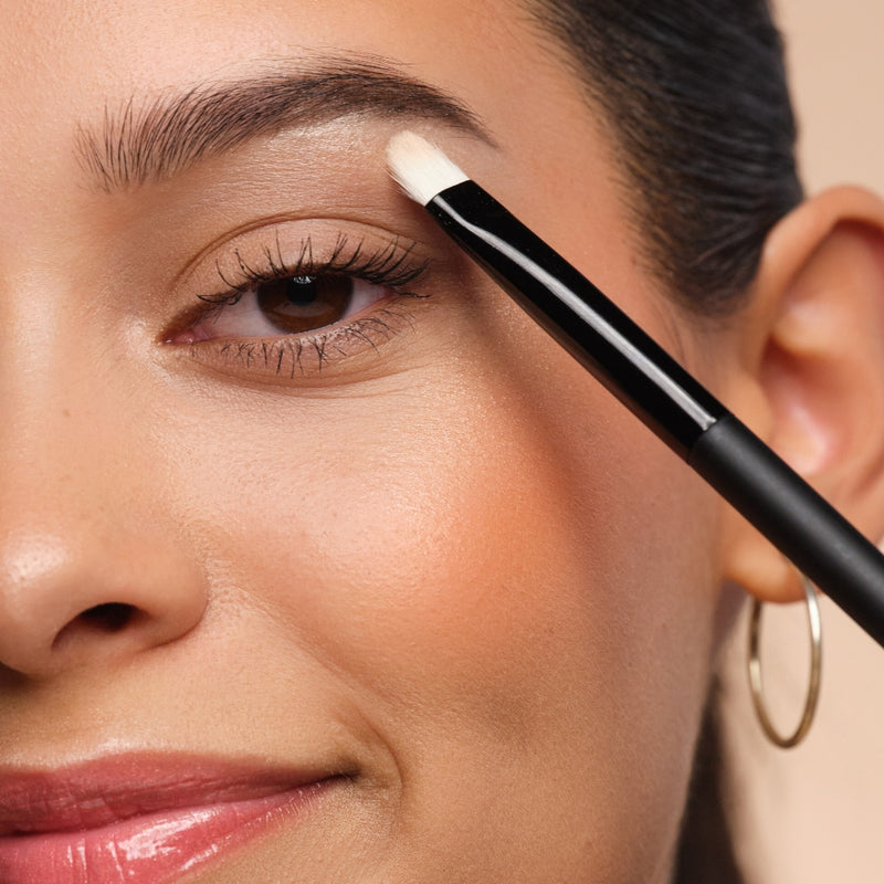 Female face with an eyeshadow brush held to the eyelid.