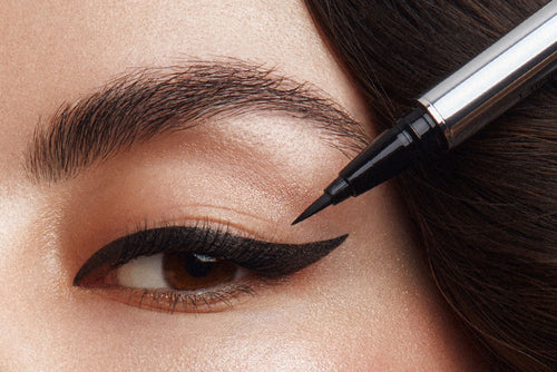An eyeliner is held in front of a made up eye