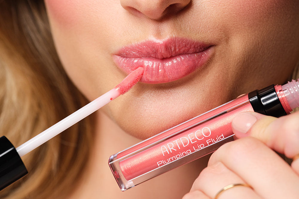 A female person holds a lip gloss in front of her lips