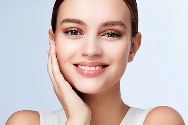 A smiling woman touches her cheek