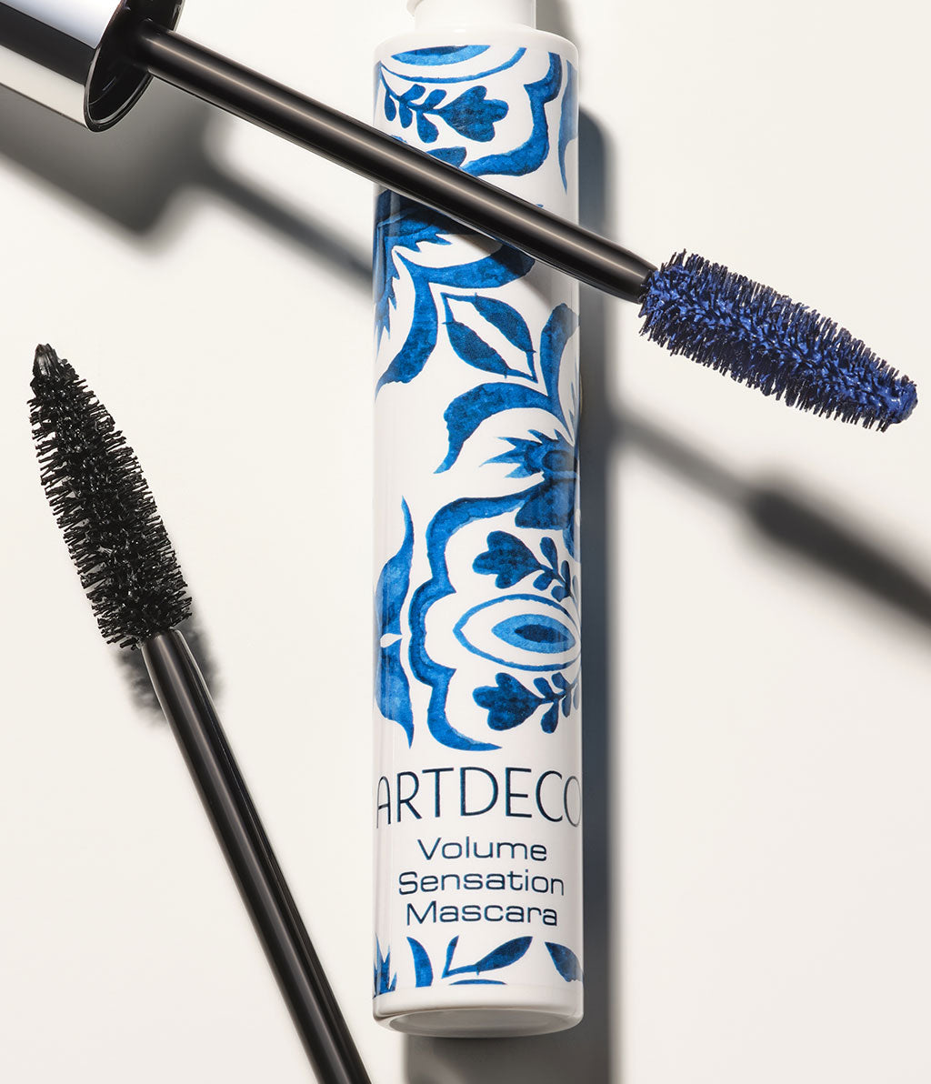 [Alt-Text:] Artdeco Volume Sensation in white with a blue Azulejo design. Two brushes with different textures, one with black and one with blue mascara, on a light background