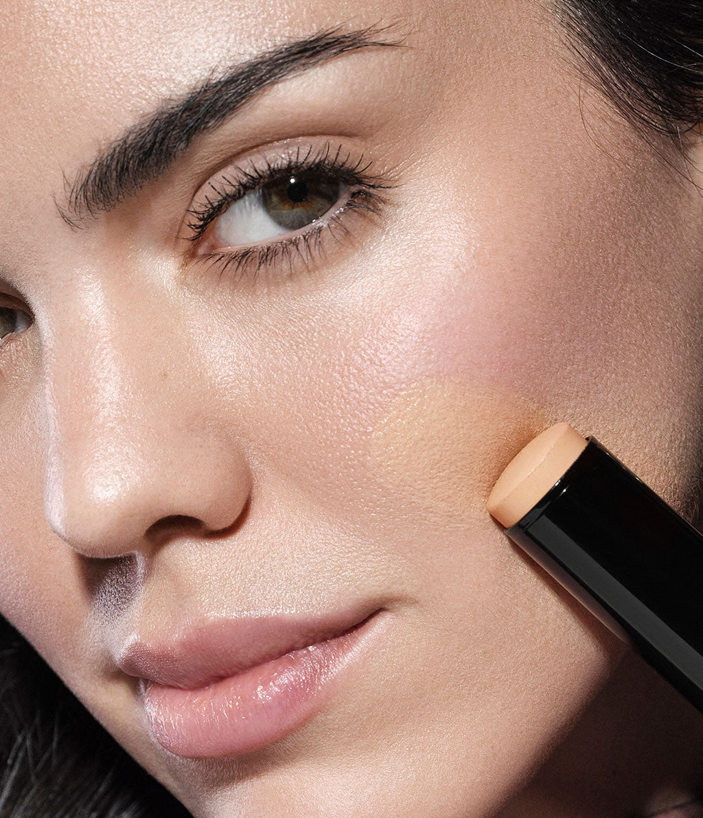 Close-up of the model's face with the new Skin Perfecting Face Stick applied to her cheek. The texture is still visible on the cheek as it has not been blended.