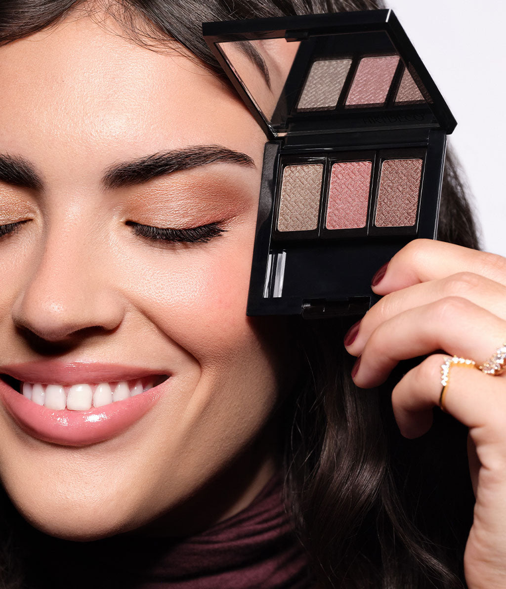 A brunette model holds the open beauty box containing the eyeshadows from the collection next to her Eye-Make-up.