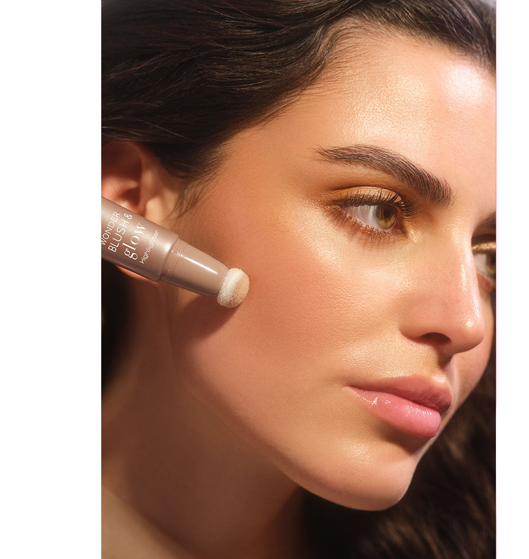 Brunette model applies the Wonder Blush & Glow Highlighter to her cheek with the sponge applicator to create a glowing makeup look.