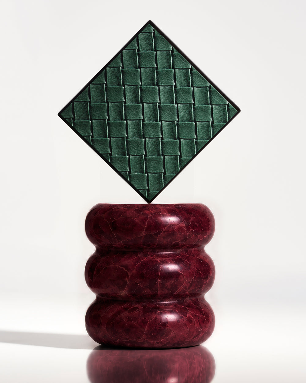 A limited-edition beauty box in the Intrecciato design, placed on a red marble pedestal.