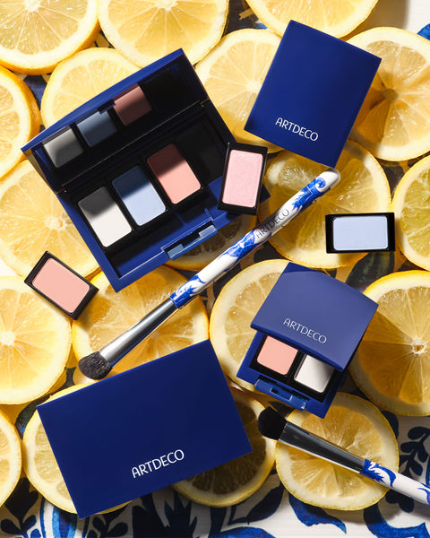 Various Beauty Boxes in a limited edition blue design presented on a background with fresh lemon slices. The scene is highlighted by individual eyeshadows in shades of pink and blue, as well as a brush with an Azulejo tile design.