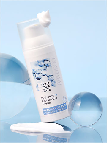 Hyaluronic + Replumping Cream on a light blue background surrounded by different-sized glass beads. There is a dab of cream on the lid.