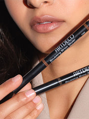 The two colors of the Sculpting Brow Styler are held in front of the model's face.