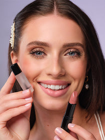 A dark-haired model holds Magix Fix and previously applied lipstick to her lips and smiles into the camera.