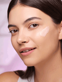 Brunette model standing sideways while Collagen Master Cream is applied to her cheek