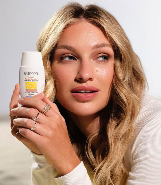 Blonde model holding the Tinted Aqua Serum Daily Defense SPF50+ in her hand