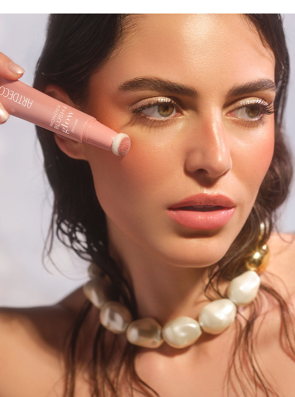 Brunette model applies Wonder Blush & Glow Rouge to her cheek with the sponge applicator to create a fresh, natural, glowing complexion.