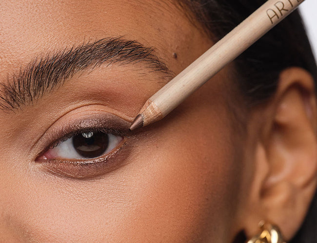 Close up on the eye of the model, holding a brown Kajal Liner against her upper lash line 
