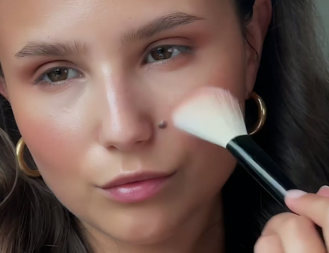 Model applies pink blush to her cheeks to give her latte makeup a fresh fall look.