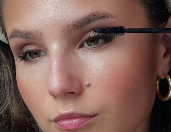 Model applies mascara to her upper lashes for a soft yet defined latte look.