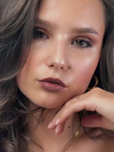 Model made up with latte makeup gently holds her hand to her face.
