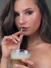 Model made up with latte makeup drinks a matching latte macchiato with a straw.