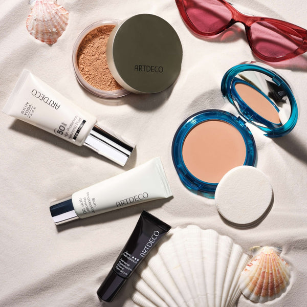 Artdeco products with sun protection and other summer items, such as sunglasses and shells placed on a sandy background.