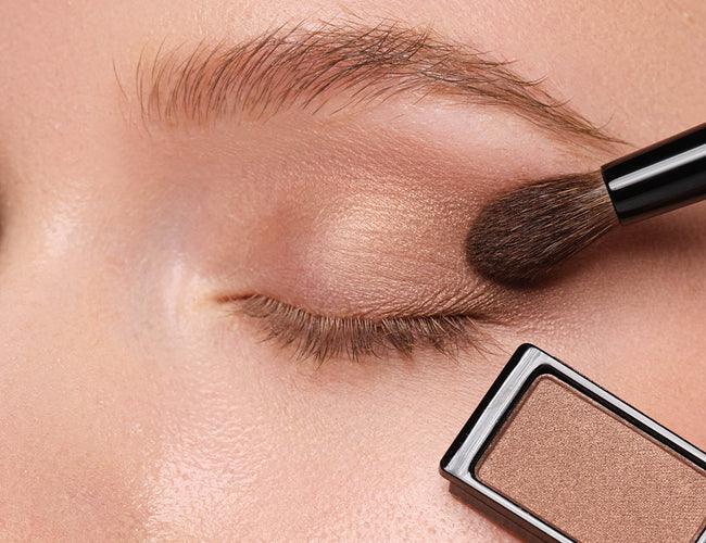Close-up of the model’s eye, to which a brown eyeshadow is being applied using a fluffy eyeshadow brush