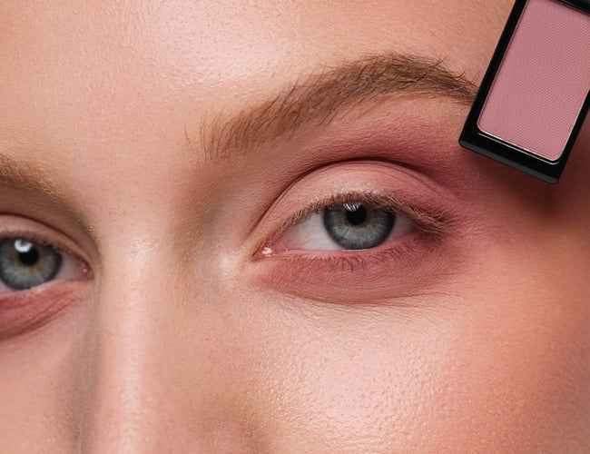 Close-up of the model’s eye, to which a berry-toned eyeshadow is being applied to intensify the eye makeup