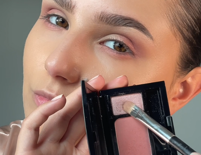 Model applies a light pink eyeshadow onto a flat eyeshadow brush.
