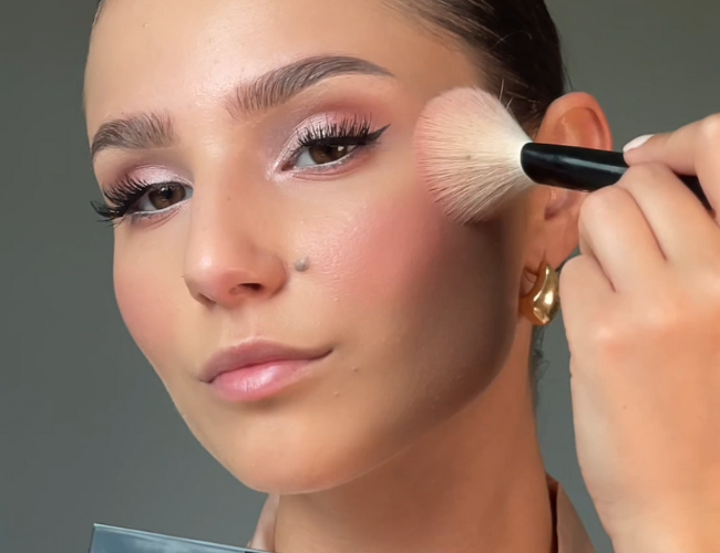 Model applies blush to her cheeks using a fluffy brush.